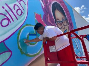 A photo of an artist painting a mural in memory of student Jailah Silguero.