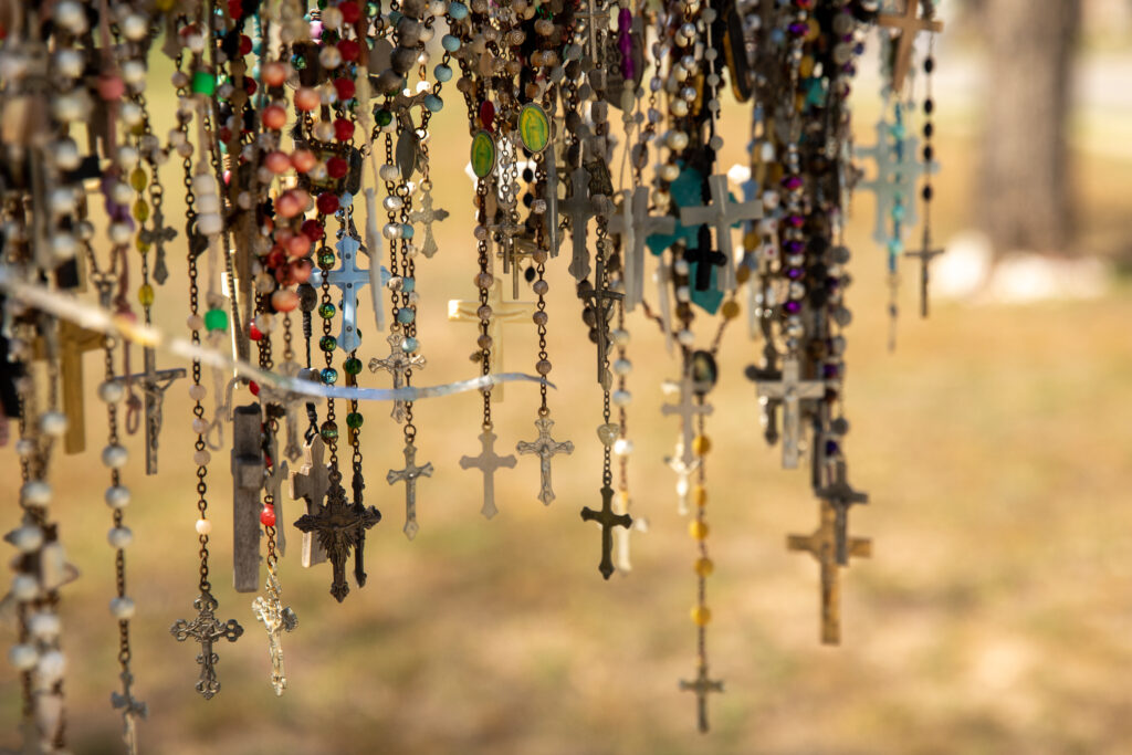 A close-up photo of dozens of rosaries hanging from a wooden cross at a makeshift memorial for the Robb Elementary shooting victims.