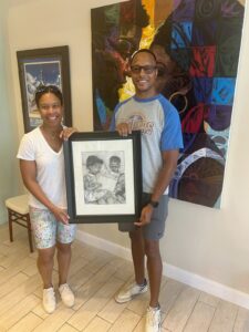 Two adults pose with a black-and-white piece of art featuring two children.