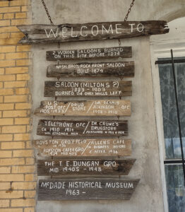 A carved wooden sign reads "Welcome To" and underneath it are several more wooden signs reading what the museum location has been over the years -- from saloon to museum.