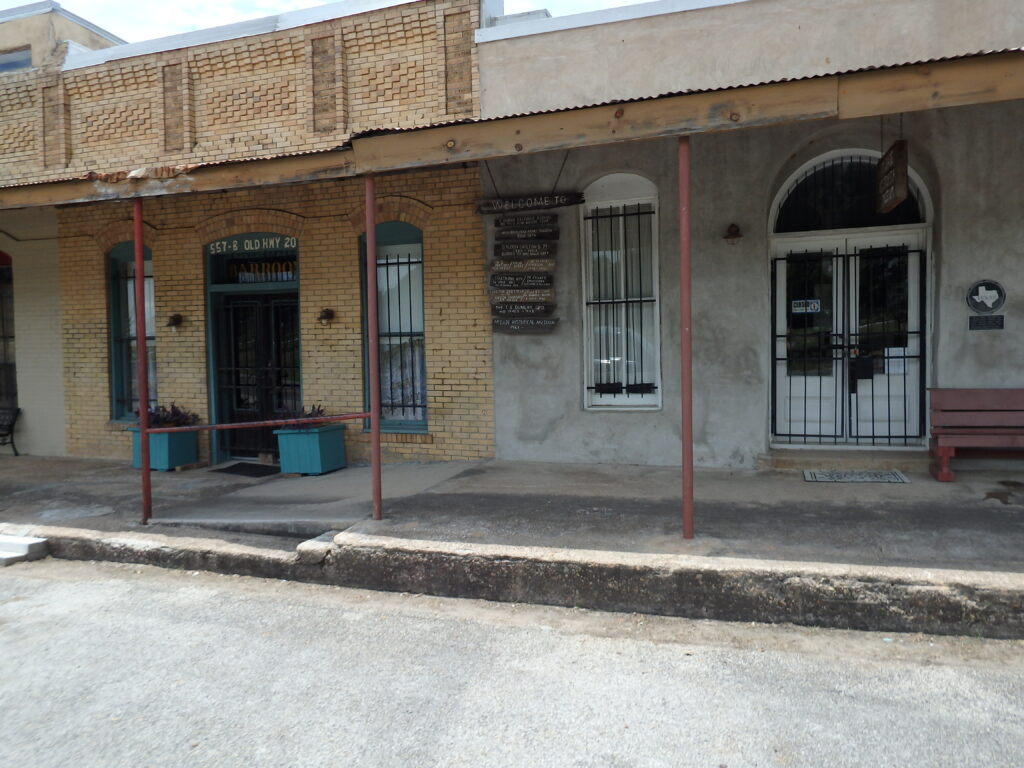 An outside photo of the museum shows a one-story brick and concrete building with a long front porch and barred windows.