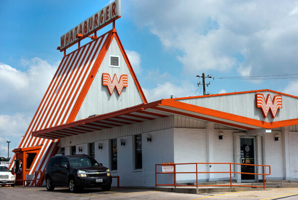 An exterior shot of a Whataburger restaurant with a dark SUV in the drive-thru